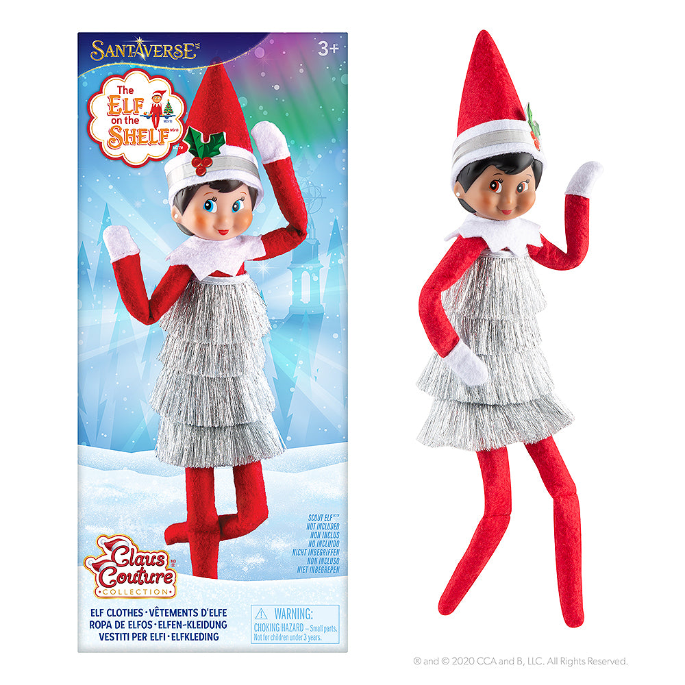 The Claus Couture Collection® Tiny Tinsel Dress packaging (left-hand side) next to a Scout Elf modeling the dress (right-hand side).