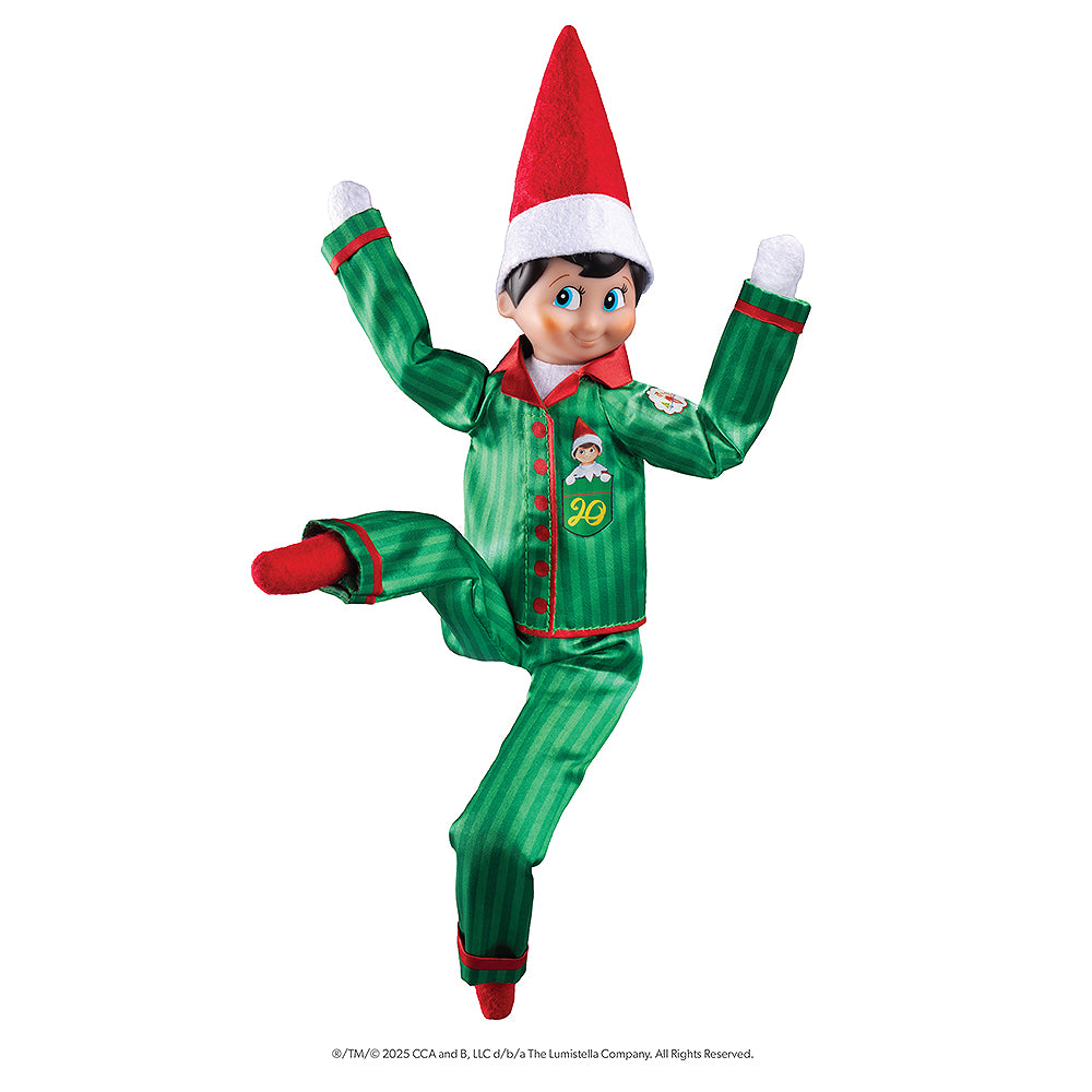 The adoptable boy limited-edition 20th anniversary Scout Elf® with blue eyes and flexible bending limbs for even easier elf scenes, donning the limited-edition luxury satin long pajama set, posing in a silly karate-like stance.