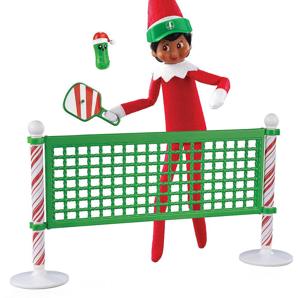 A girl Scout Elf playing pickleball with the Polar Props™ Pickleball Play Pack. She is taking a swing at the festive pickle at the net.
