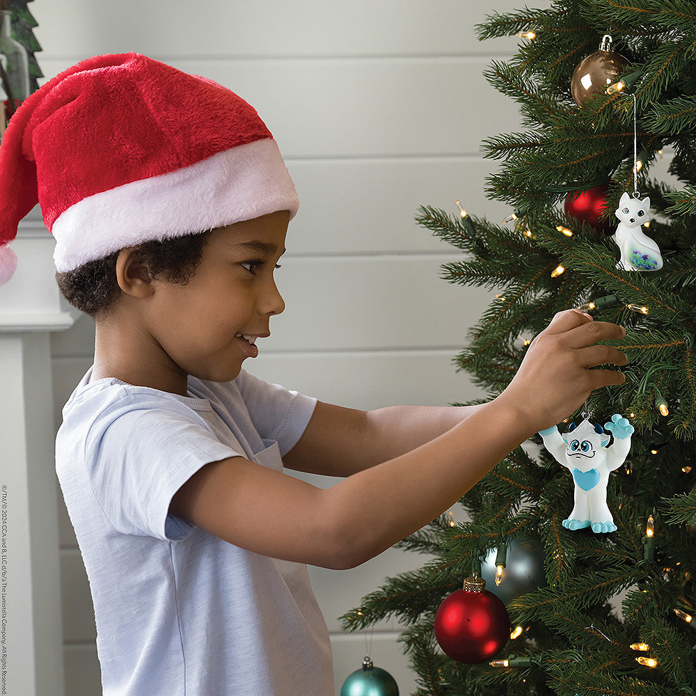 Little boy hanging the SnoBiggie™ Yeti ornament on the Christmas tree from the Santaverse™ Ornament Collection