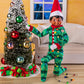 A scene of a boy Scout Elf donning the Claus Couture Collection® Goodnight, Sleep Bright PJs while wrapping Christmas lights on a miniature Christmas tree with ornaments and a little sofa in the background