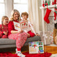 A lifestyle image of a mom and her daughter and son reading the The Elf on the Shelf®: A Christmas Tradition, Limited 20th Anniversary Edition book in their living room. They are seated on a sofa, dressed in Christmas pajamas, surrounded by vibrant Christmas decor. A Scout Elf sits on the mantle among Christmas tree decor and hanging stockings. Presents are in the foreground.