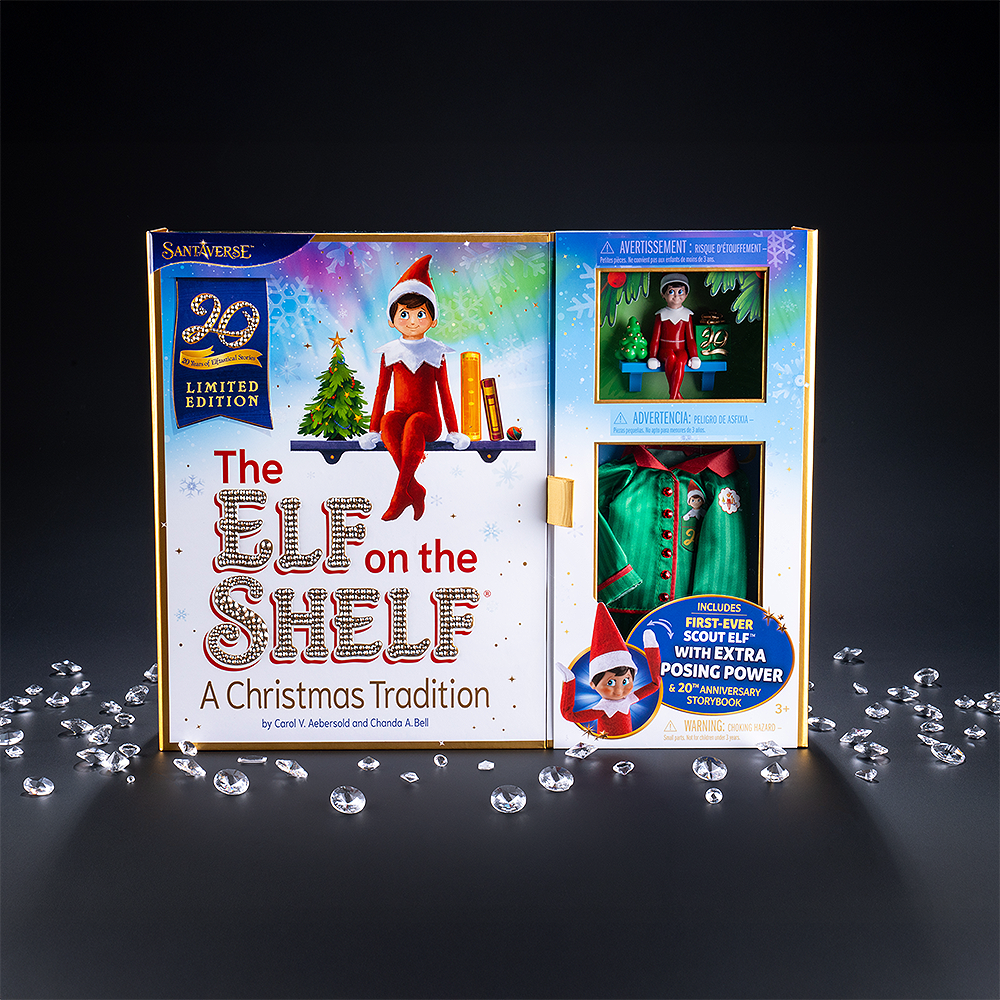 A lifestyle of the front view of the packaging of the The Elf on the Shelf®: A Christmas Tradition 20th Anniversary Sparkle Holiday Box Set. This collector's item features 4,500 Swarovski® hand-placed crystals. Some of the crystals can be seen on the cover's lettering, as well as on the buttons on the included limited-edition luxury satin long pajama set. The box set is photographed in front of a dark background with light casting a shadow. You can also see Swarovski crystals scattered around the base.