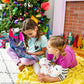 Two little girls read Elf Pets: An Arctic Fox Tradition by their colorful Christmas tree