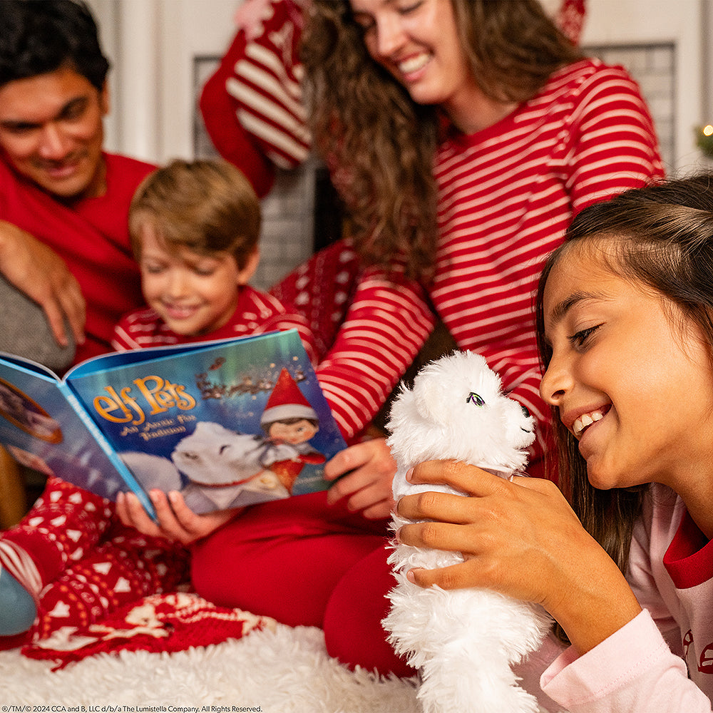 A family reads Elf Pets: An Arctic Fox Tradition together, the little girl snuggles the Arctic Fox plush