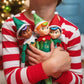 A little boy in Christmas pajamas snuggling the Elf Mates® Chef, Cobbler and Toy Maker dolls with a Christmas tree in the background