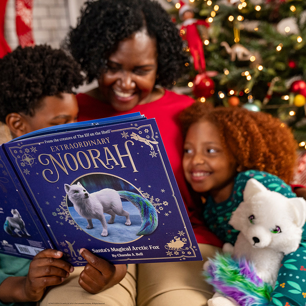 Family gathered around the Christmas tree reading xtraordinary Noorah: Santa’s Magical Arctic Fox Book, the little girl is holding a Noorah™ Plush