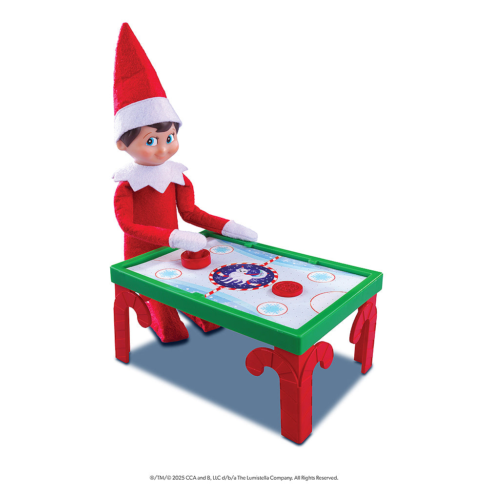 A Scout Elf is posed with a festive air hockey table that is included in the Polar Props™ The Official Elf Ideas Fun & Games Kit.