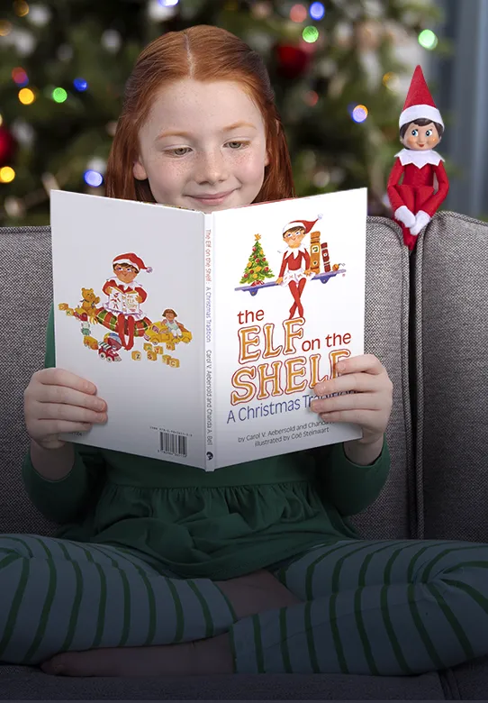 A girl reading The Elf on the Shelf storybook while sitting on a sofa. Next to the girl on the back of the sofa sits a girl Scout Elf. Behind the sofa is a Christmas tree.