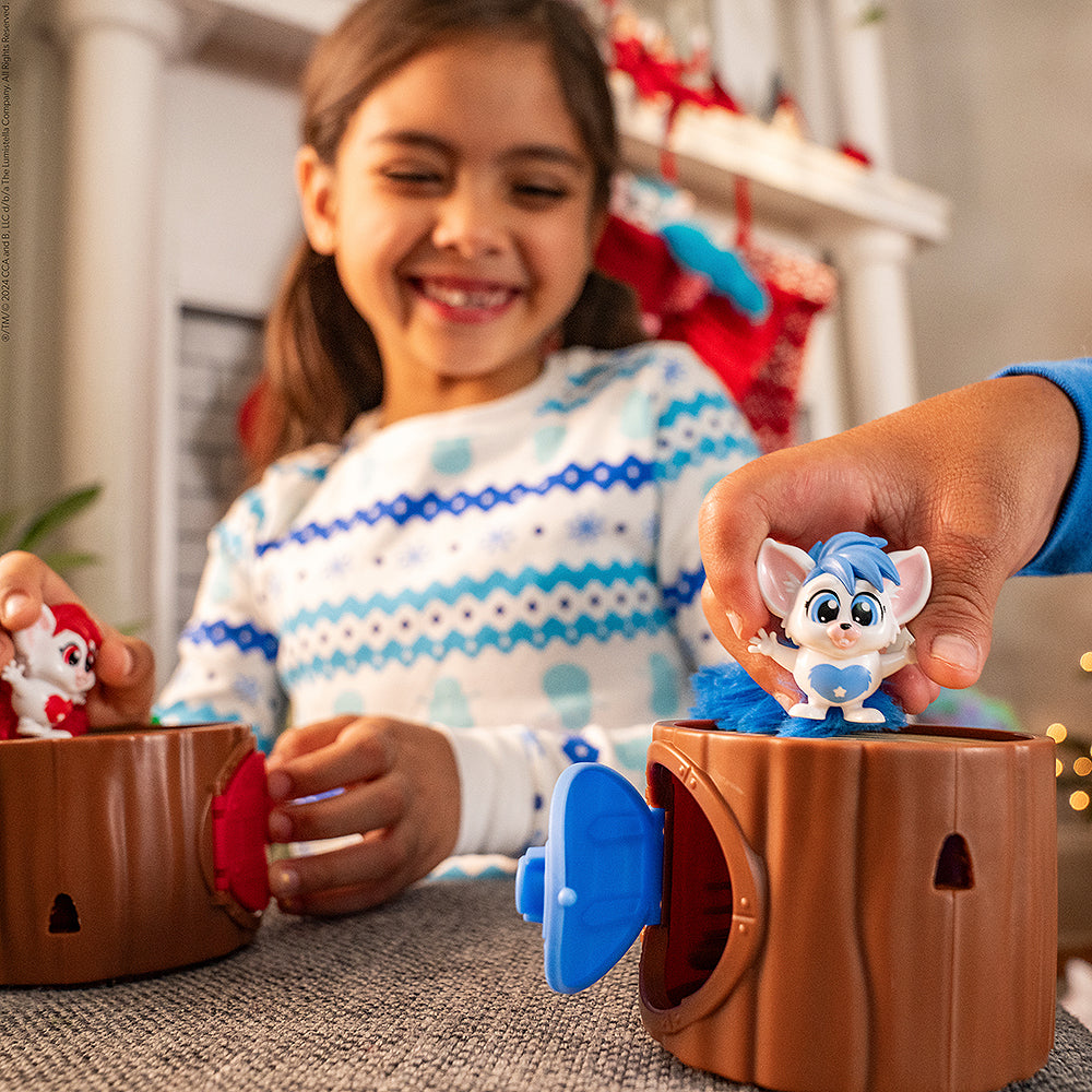 A girl playing with the red Bogie™ Hideout Surprise and another friend playing with the blue Bogie™ Hideout Surprise with a fireplace and stockings hanging in the background