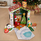 A lifestyle image of The Elf on the Shelf® DIY Elf Cottage, with a Scout Elf® and Elf Mates® Toy Maker posing together. The Cottage is set up on the floor in front of a festive Christmas tree and other decor.