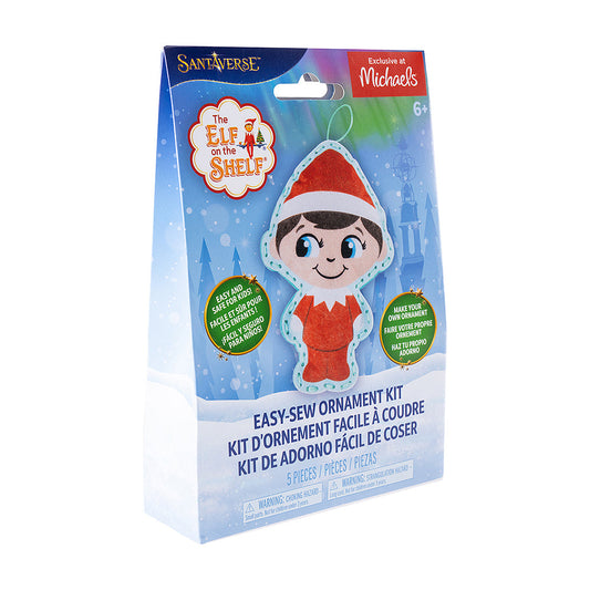 A front view of the packaging of The Elf on the Shelf® Easy-Sew Ornament Kit, which is slightly turned to the right. The packaging has the finished product, The Elf on the Shelf and Santaverse logos and other details. The packaging also has an "Exclusive at Michaels" label on it in the top right-hand corner. The background is a vector background commonly associated with the Santaverse brand, featuring conifer trees, light bursts, snowflakes, the Northern Lights, and a snow-covered landscape.