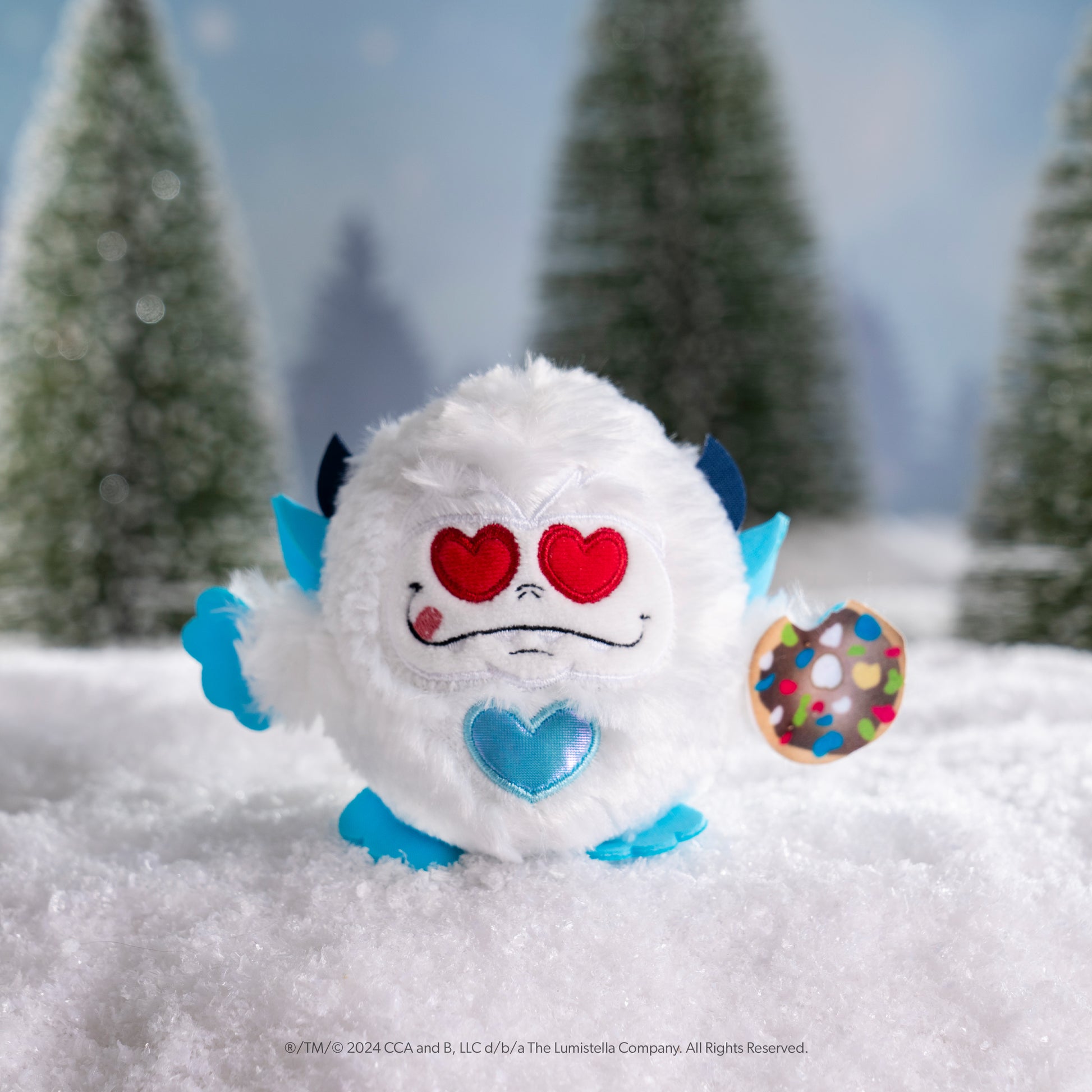 SnoBiggie™ Yeti SnoBall Surprise plush with donut and heart eyes in a snowy forest