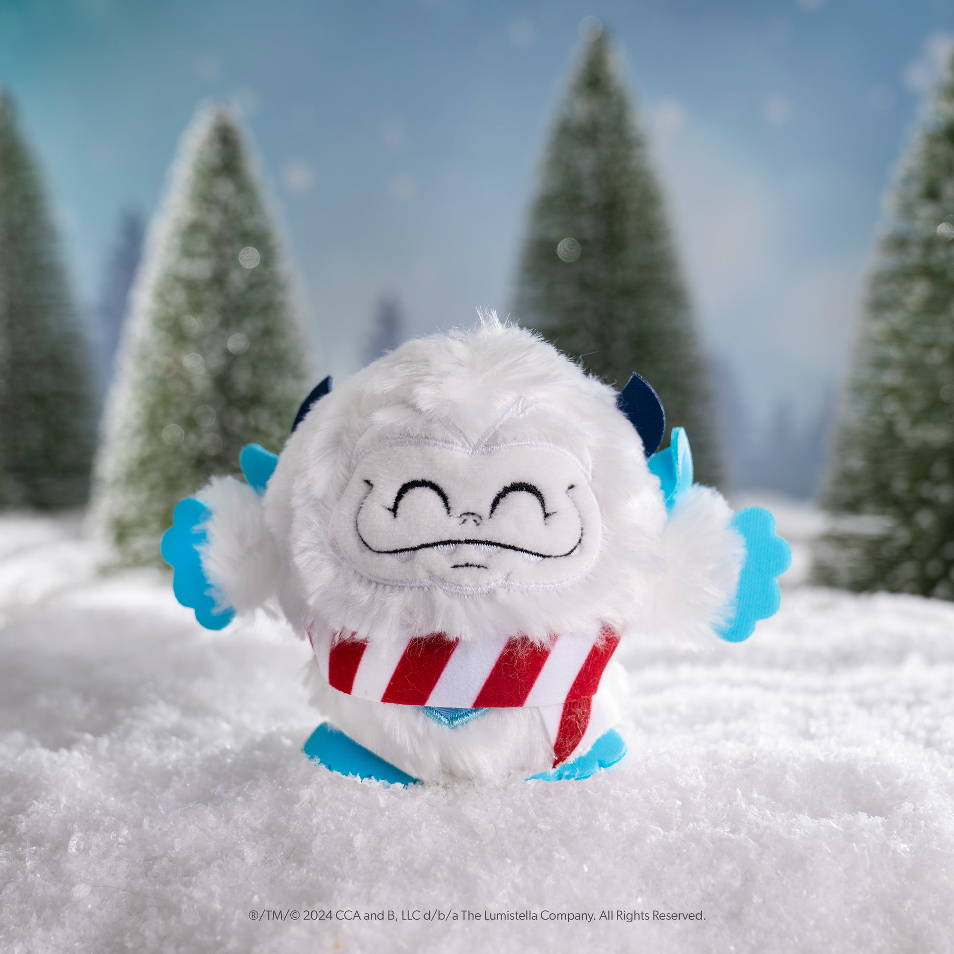 SnoBiggie™ Yeti SnoBall Surprise plush with candy cane pattern scarf in a snowy forest