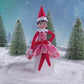 A girl Scout Elf® sitting in a snowy forest donning the Claus Couture Collection® Pink Peppermint Party Dress, spinning around in this product video to give customers a 360 degree view of the product