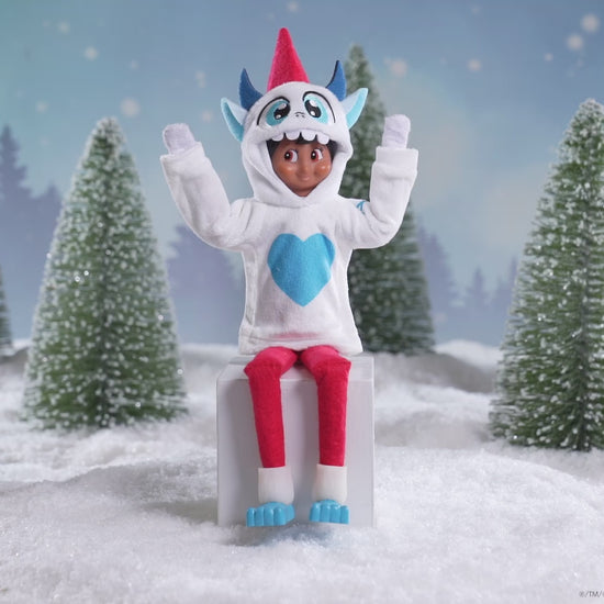 A Scout Elf® sitting in a snowy forest donning the Claus Couture Collection® Yeti Hoodie Set, spinning around in this product video to give customers a 360 degree view of the product